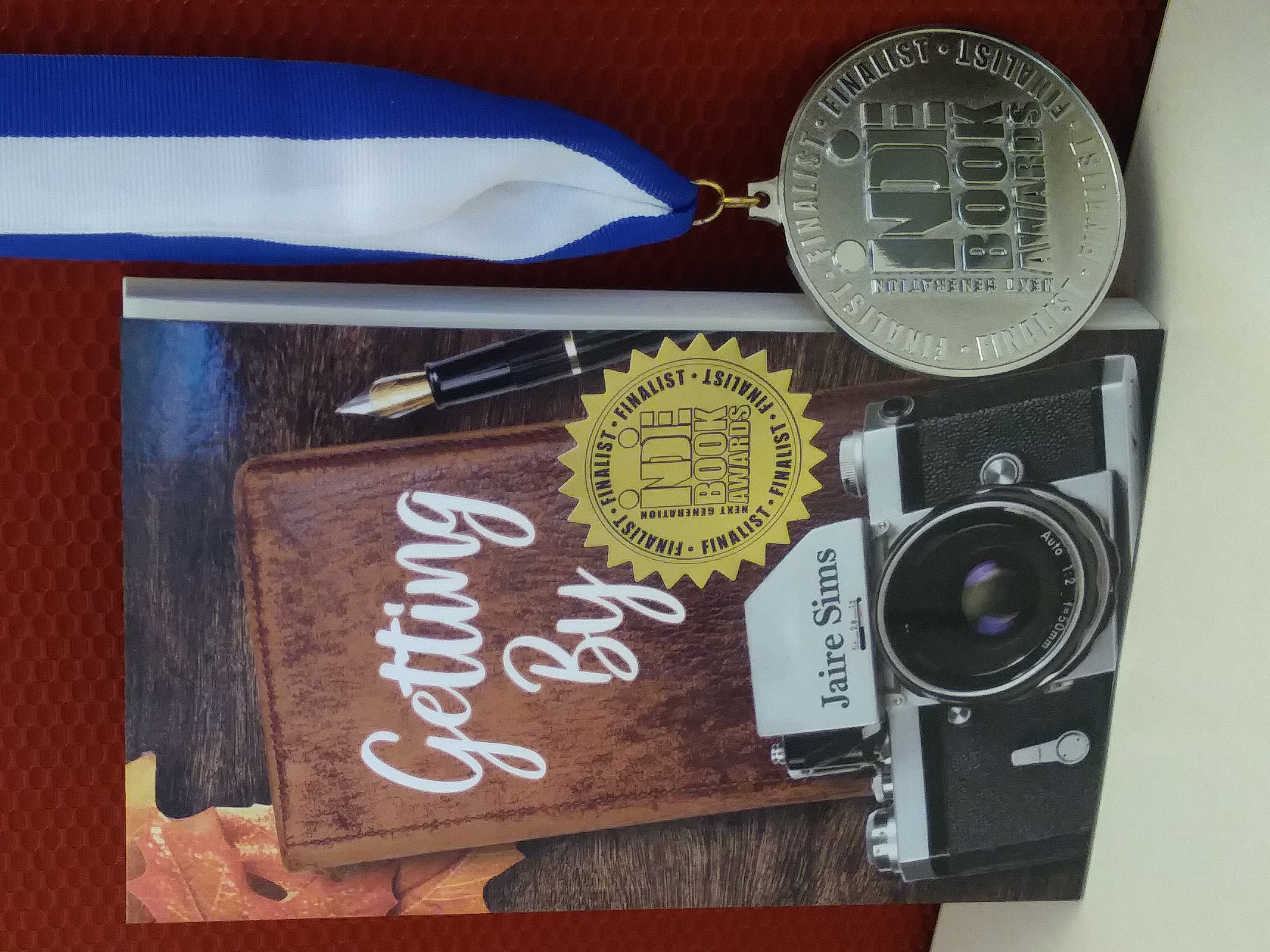 A copy of the book, Getting By, with an award sticker on the cover. Next to the book is a medal. 