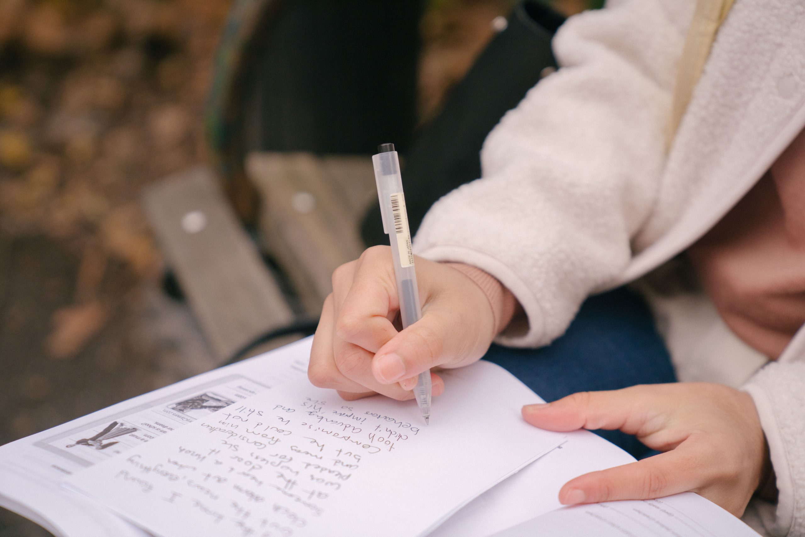 A person writing on a notebook while sitting on a bench.