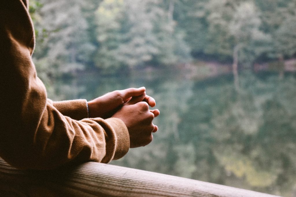 A person resting their arms on a bridge rail while looking out into the water. 