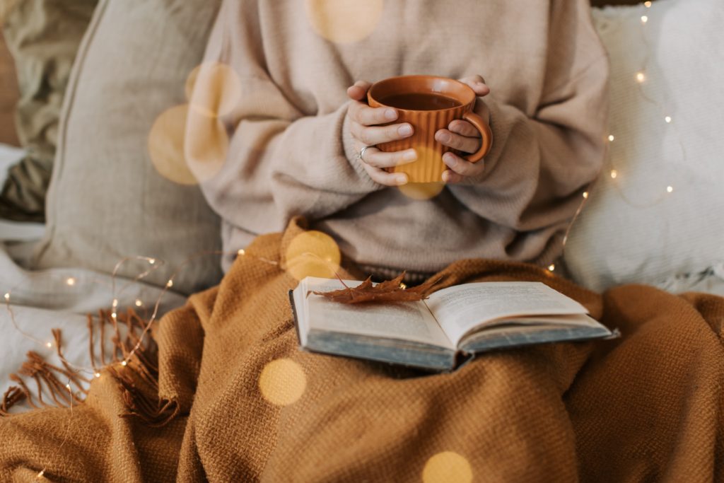 A person reading a book with a hot drink in their hand. 