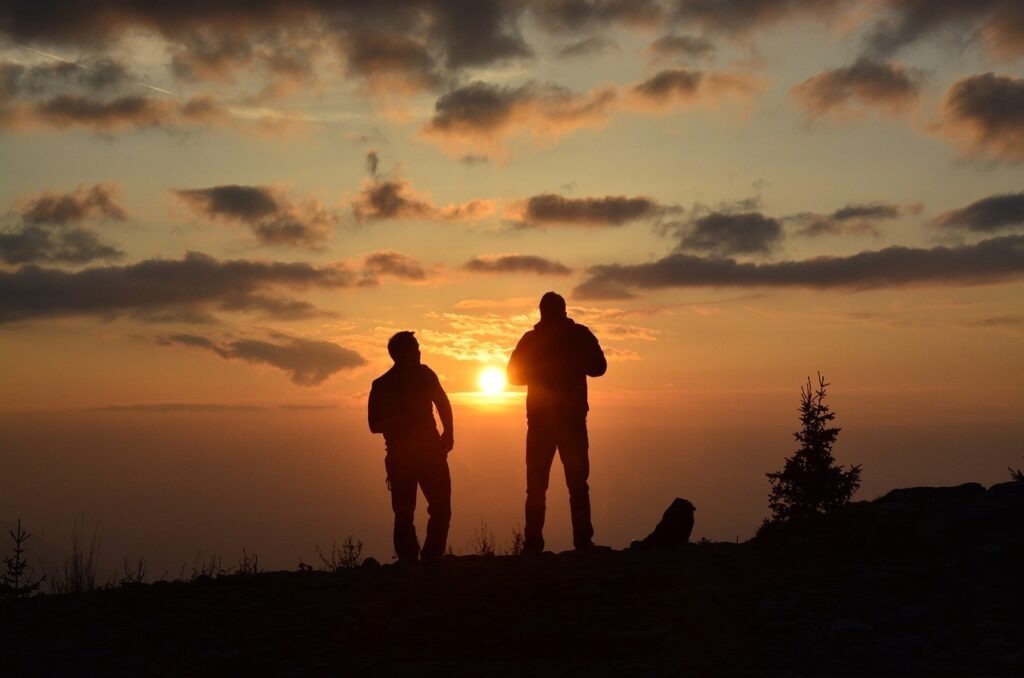 Two men looking out into the sunset from a hill.  