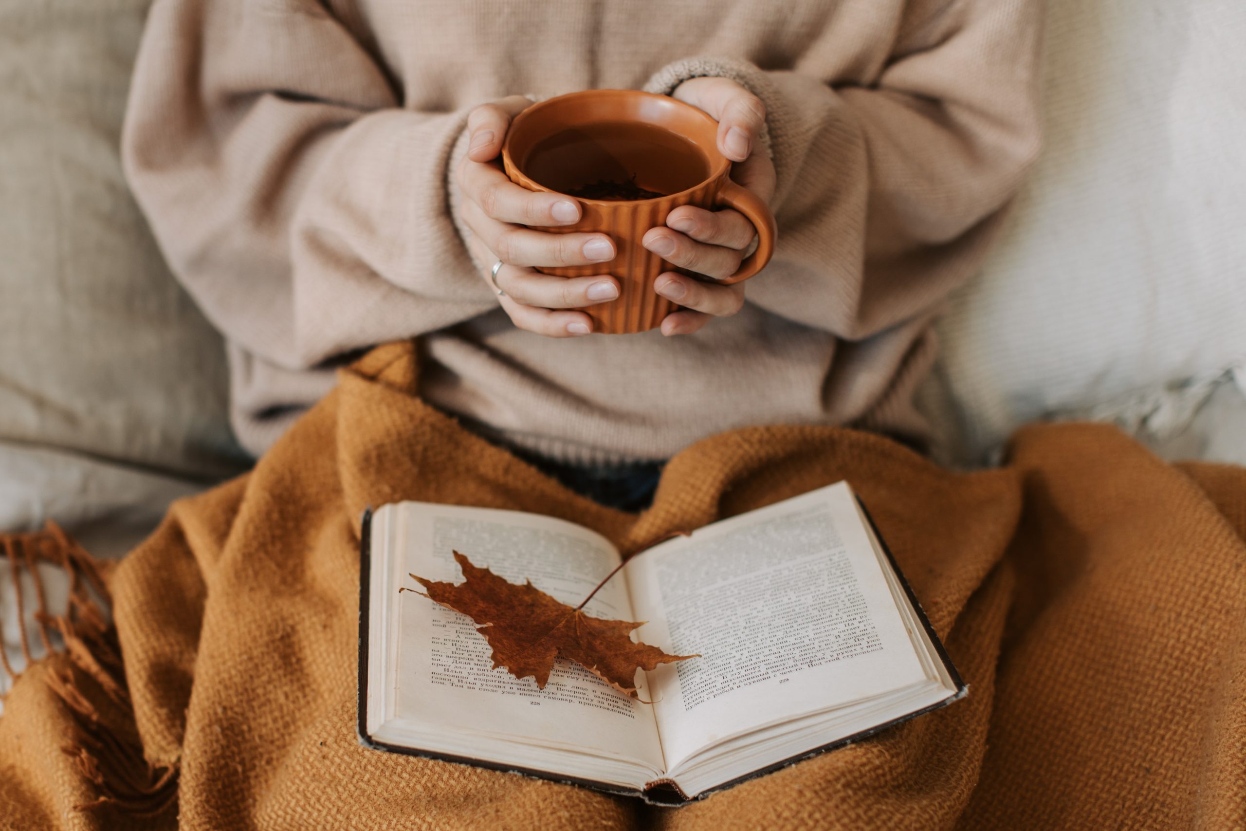 A person reading a book on their lap while holding a drink in their hands.