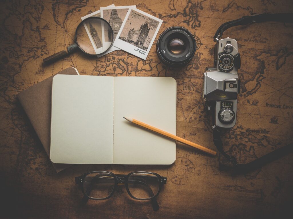A blank notebook, a camera, a pair of glasses, and a few photographs. 