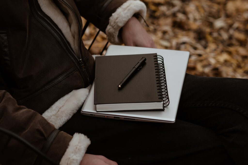 A notebook, pen, and laptop on top of a man's lap.  