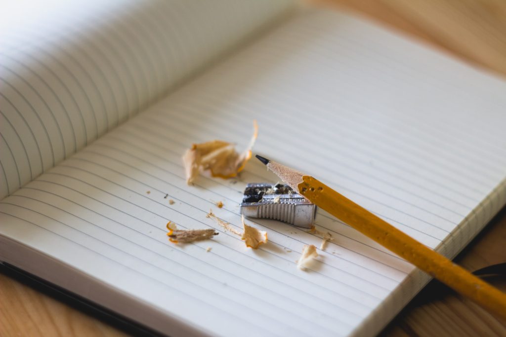 An open notebook with a pencil and pencil sharpener on top. 