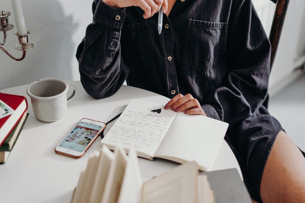 A person sitting on wooden chair writing content on a notebook.
