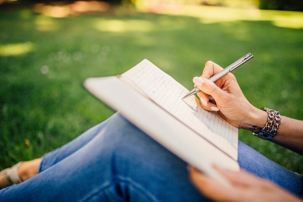 A person writing on a notebook outside on the grass. Knowing the appropriate word count for your story is one of the best things to consider when writing a young adult novel. 