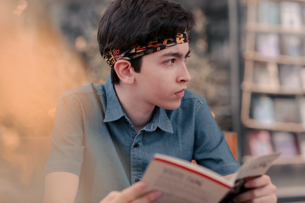 A young boy holding a book in his hands. Knowing what matters to your readers is one of the best things to consider when writing a young adult novel. 