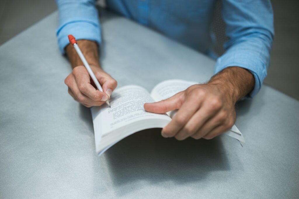A person writing notes in a YA book with a pencil.