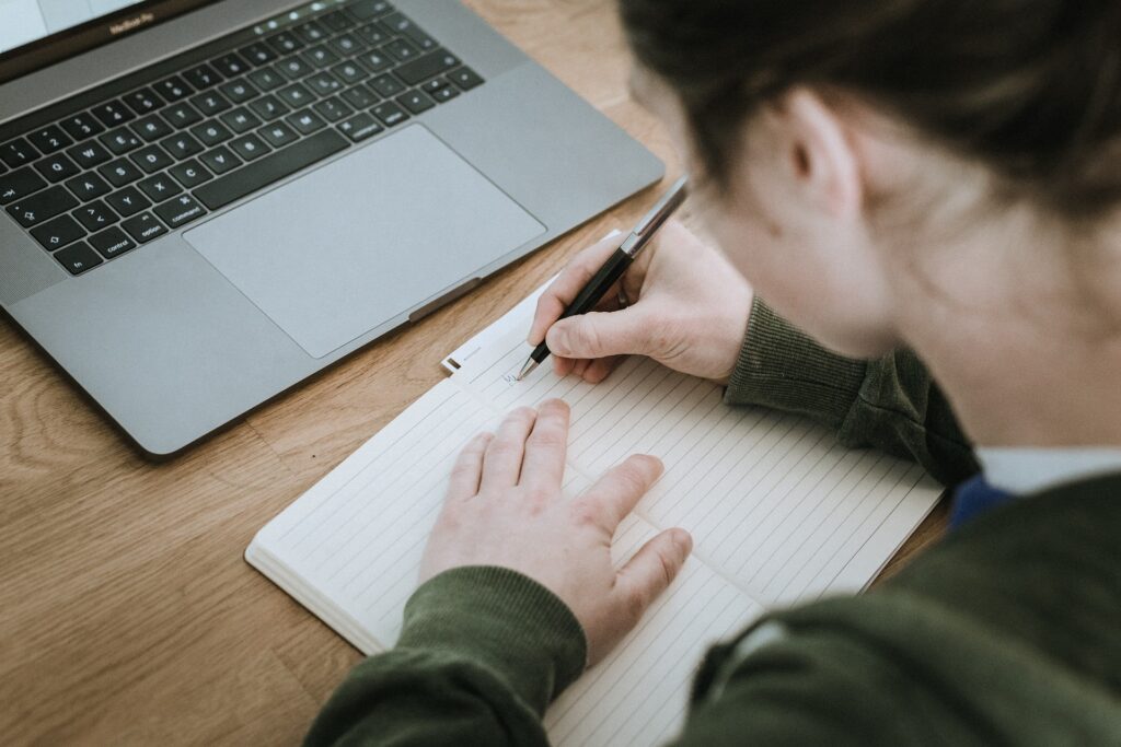 A woman writing fiction on her notebook. There is a difference between writing coming of age and young adult fiction. 