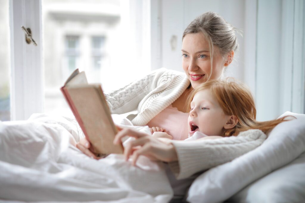 A mother and daughter reading a book with interest in bed. Universal messaging is what makes YA fiction messaging speak to all ages.