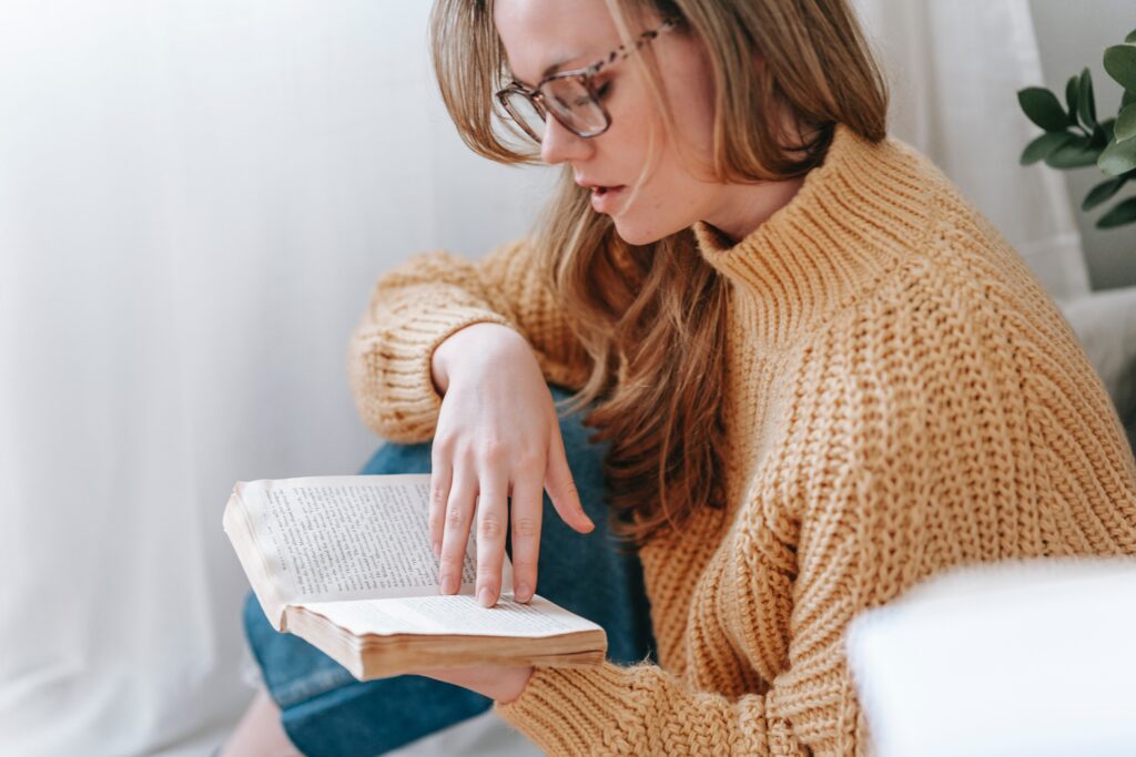 A young lady reading a YA fiction book in an apartment. 