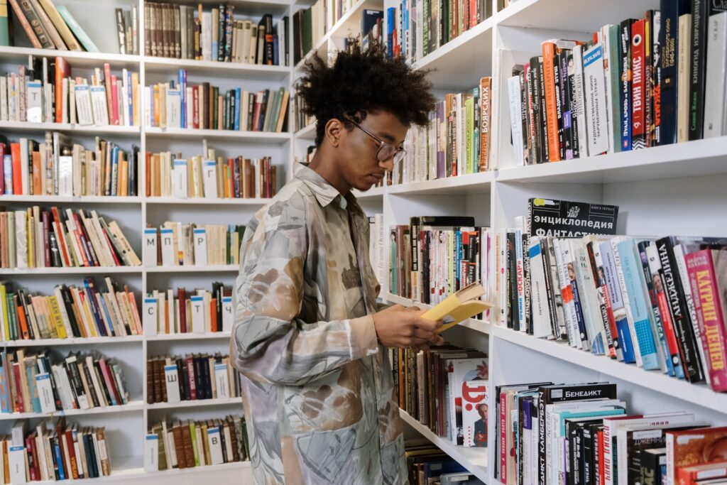 A young man reading a YA fiction book in the library. 