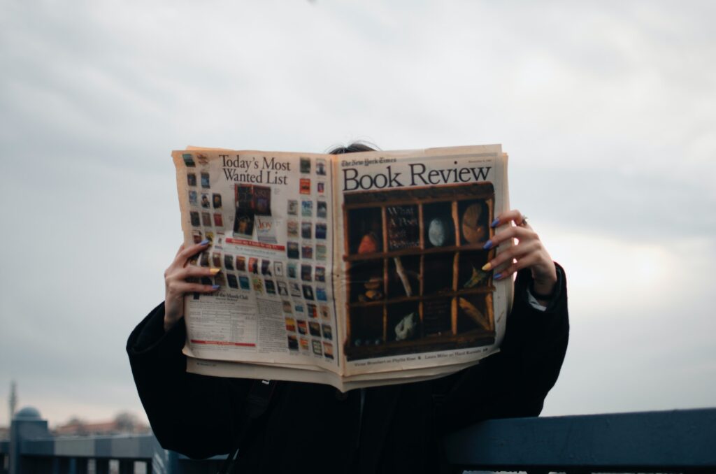 A person holding a newspaper with a book review on the cover. 