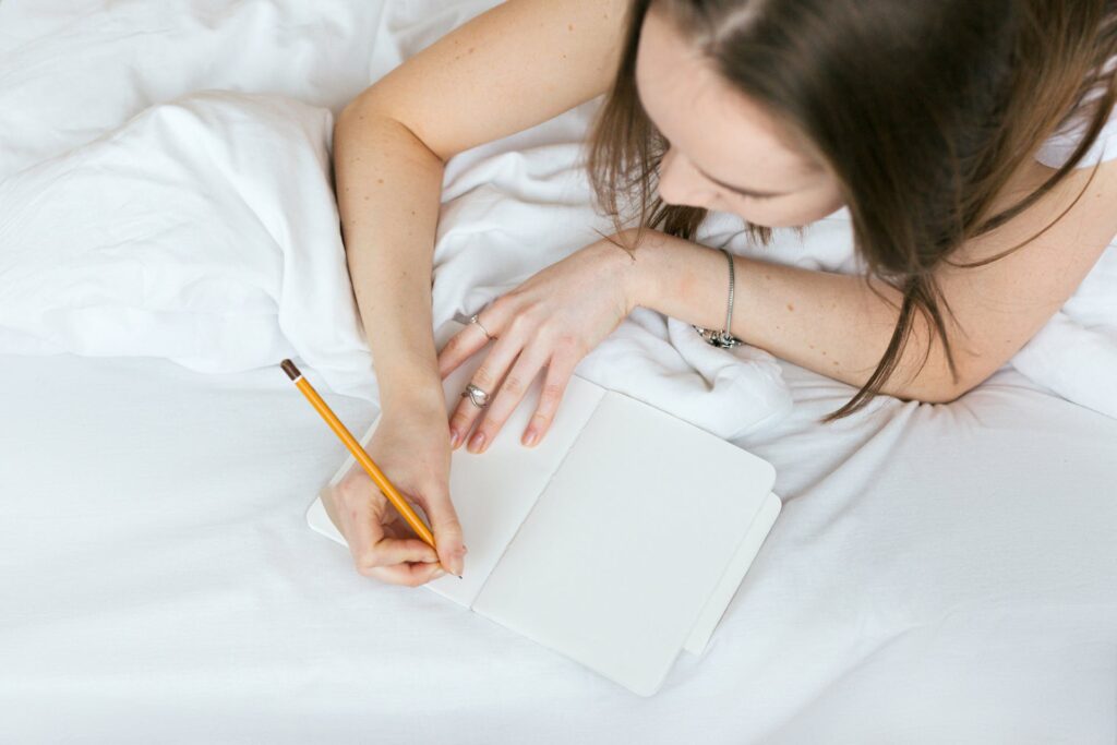 A woman writing on a notebook using a pencil.