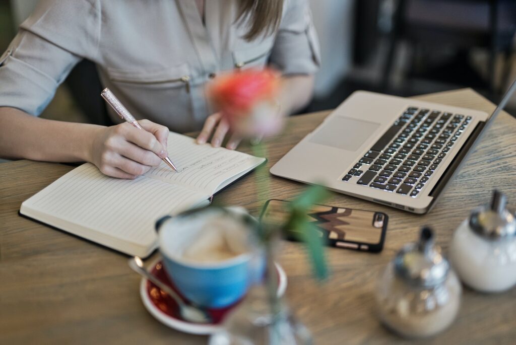 A person writing on a notebook beside a Macbook. Cultivating a creative environment is one of the strategies to overcome writer's block and fuel your creativity. 