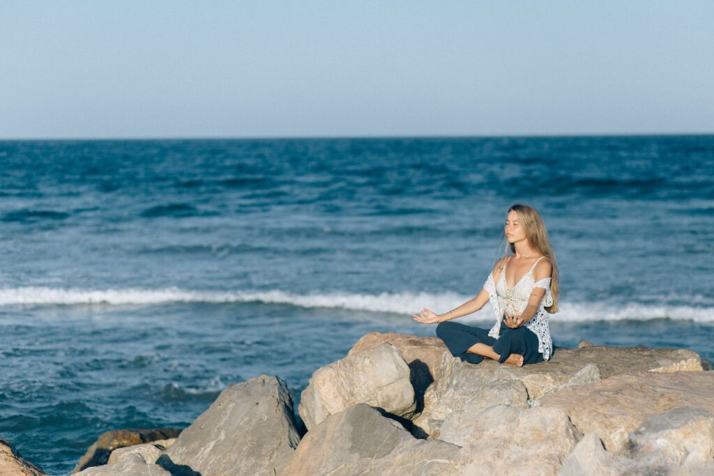 A woman meditating near sea. Finding ways to reduce stress is one of the strategies to overcome writer's block and fuel your creativity.