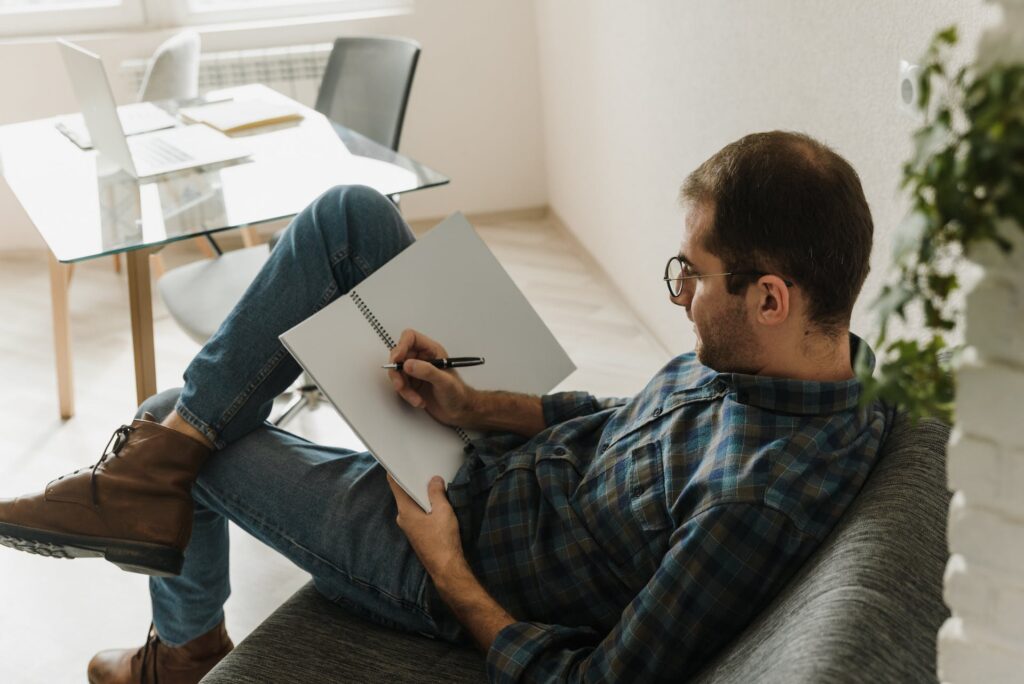 A man sitting on a sofa preparing to write. 
