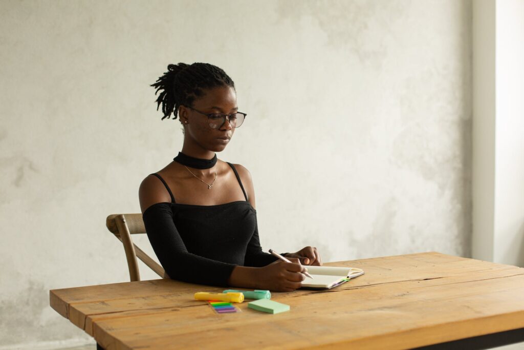 A focused woman writing notes in notebook. Crafting multidimensional protagonists is part of writing YA narratives from different points of view.