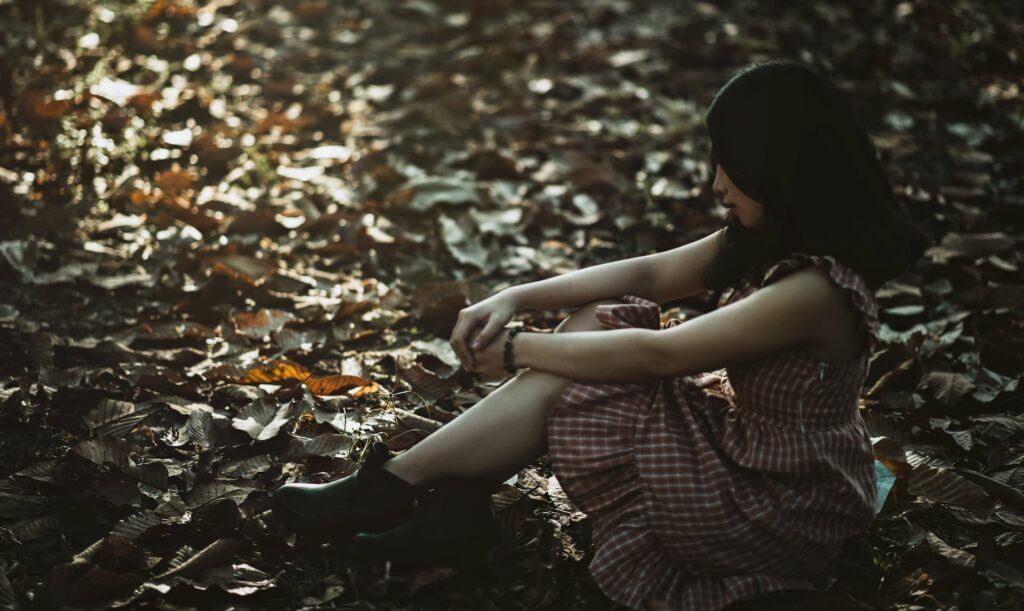 A woman sitting on the ground covered with dried leaves. You can utilize the setting and atmosphere to build tension and suspense in YA fiction.
